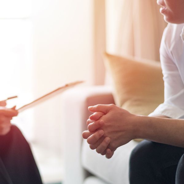 Zwei Personen sitzen sich gegenüber, eine hält ein Klemmbrett, die andere verschränkt die Hände im Schoß